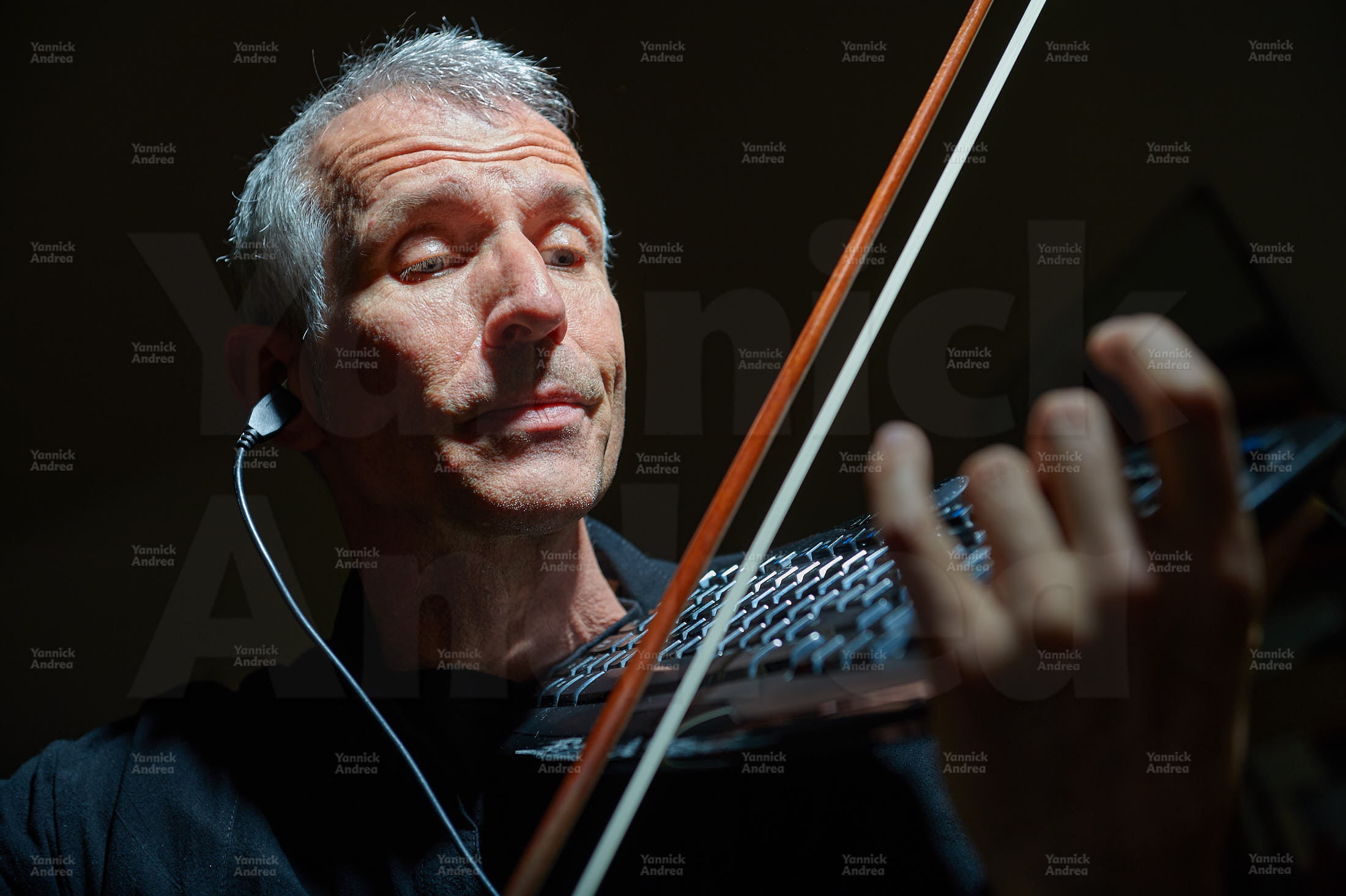 Ein Foto zur Bebilderung der Seite "Downloads". Es zeigt den Komponisten und Dirigent mit Tastatur, Geigenbogen und USB-Stecker im Ohr. Die Tastatur hält Fortunat wie eine Geige.